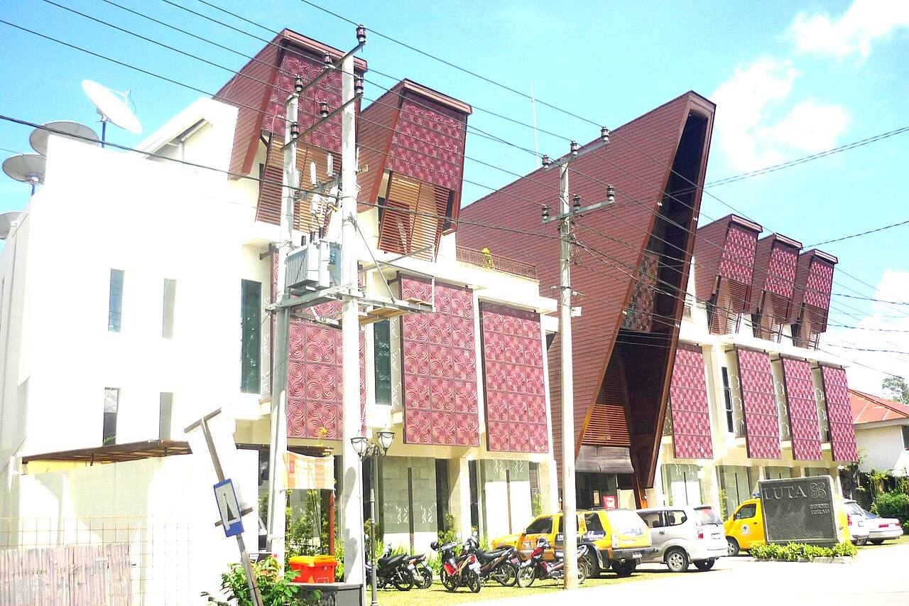 A red-and-white building with sharply sloping rooflines along a street in Rantepao