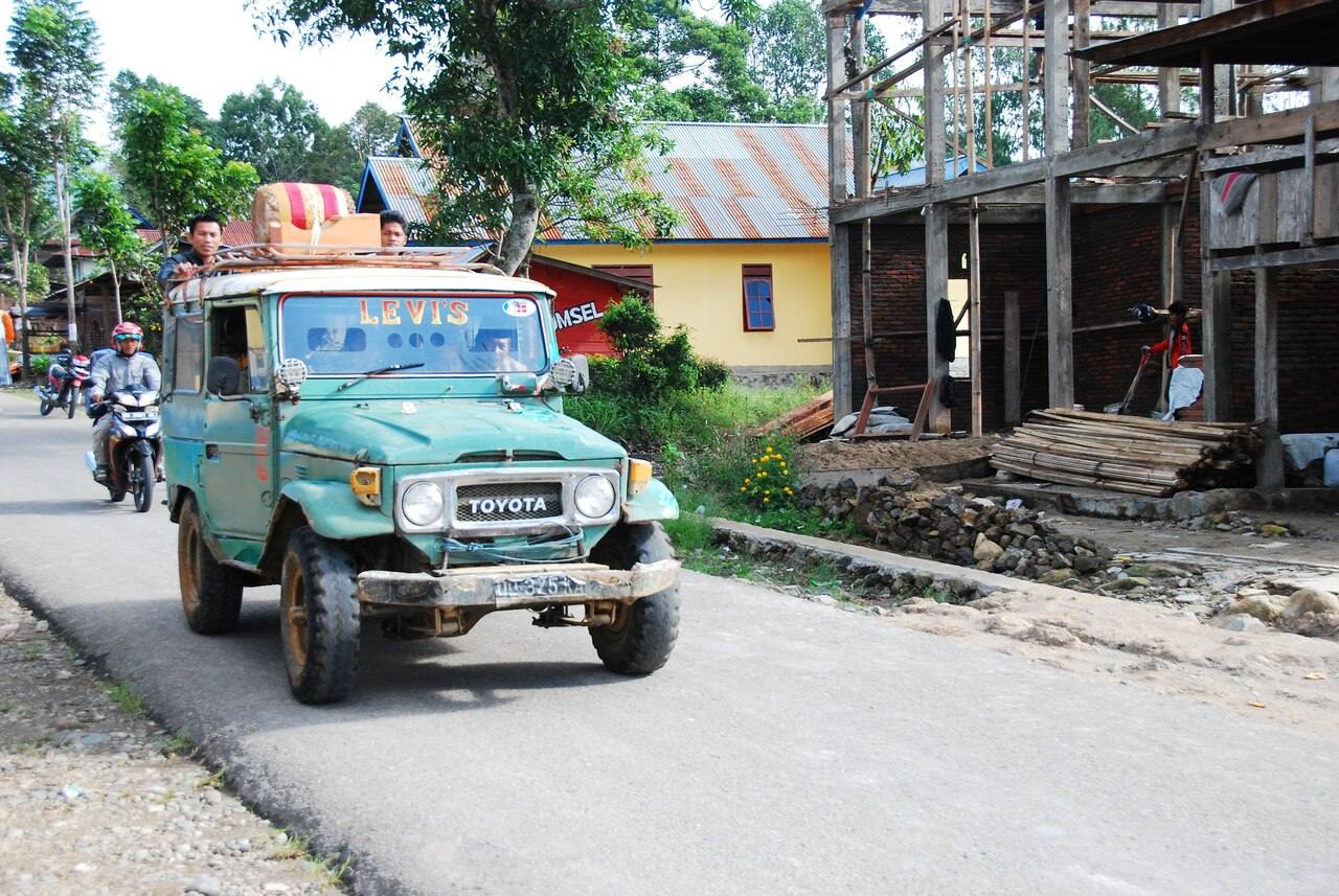 A green shared vehicle and motorbikes on a village road in Tana Toraja