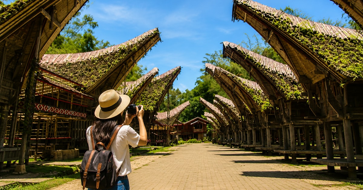 A visitor photographs rows of tongkonan buildings beneath blue sky